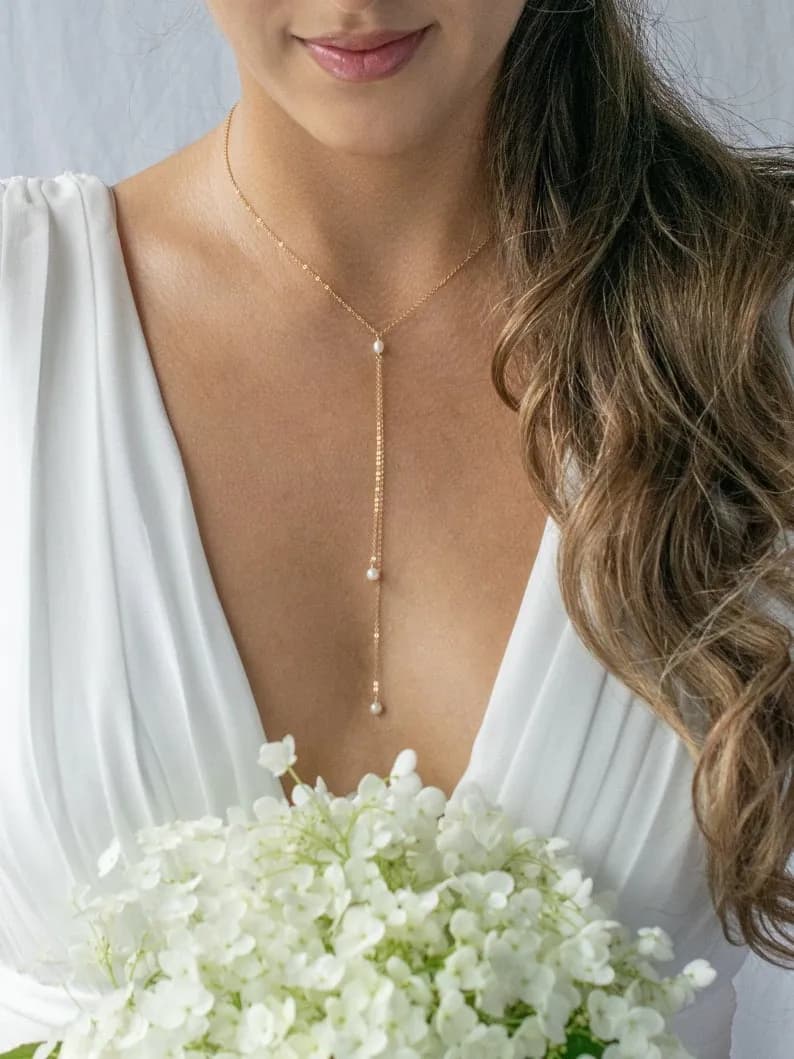 Delicate gold necklace with a long, thin chain and three small pearl accents, worn by a person with long brown hair and a white dress.