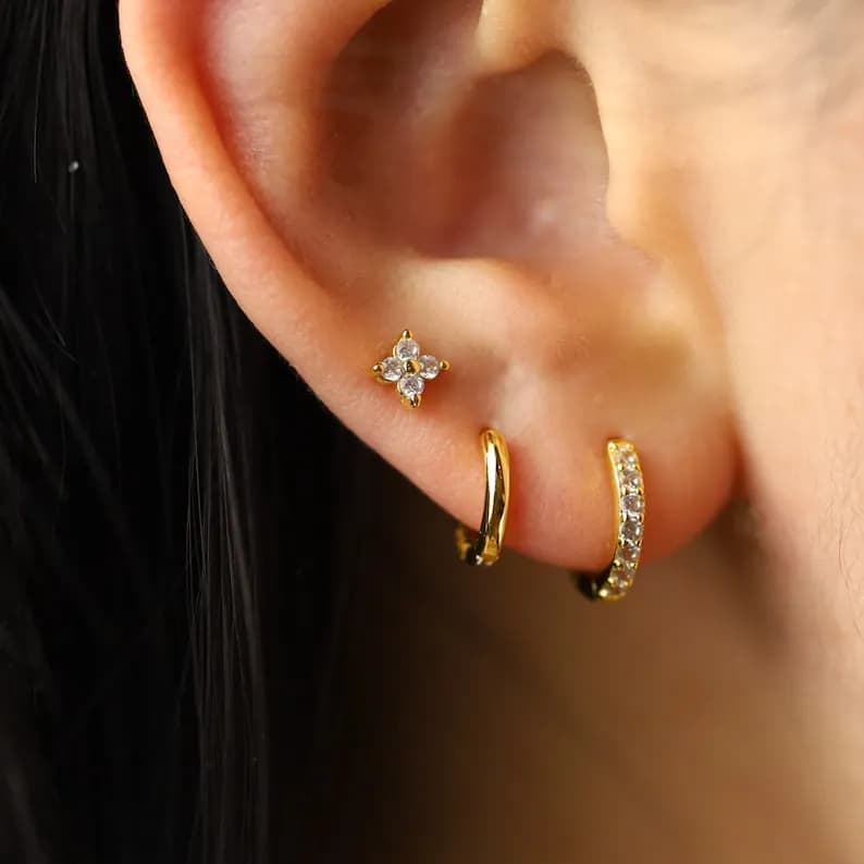 Gold earrings with small clear stones in a flower design and a hoop with clear stones.