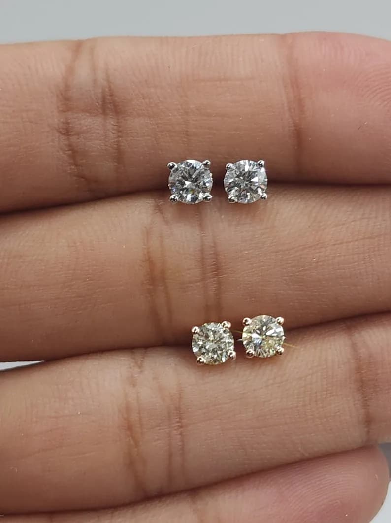 A pair of diamond stud earrings with round, clear diamonds set in gold-colored metal.