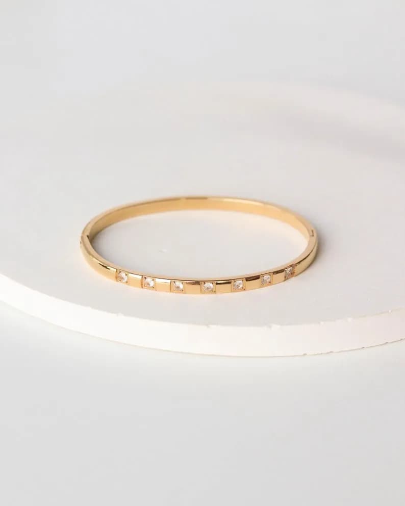 Gold bangle bracelet with clear square-shaped stones set along the edge.