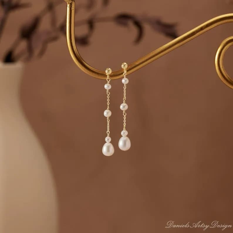 Gold-colored earrings featuring white pearl drops, hanging from a curved gold bar with a delicate design.