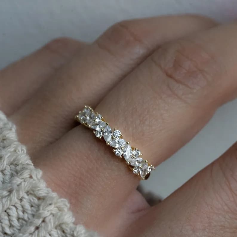 Gold-toned ring featuring marquise-cut and round-cut clear gemstones, creating a sparkling band on a finger.