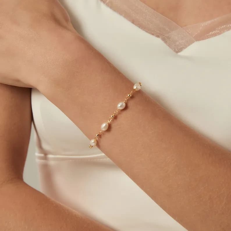 A delicate gold chain bracelet with small white pearls. The bracelet is delicate and feminine.