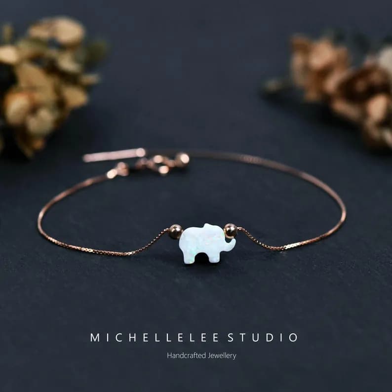 Delicate silver chain bracelet with a white opal elephant charm on a dark gray background.