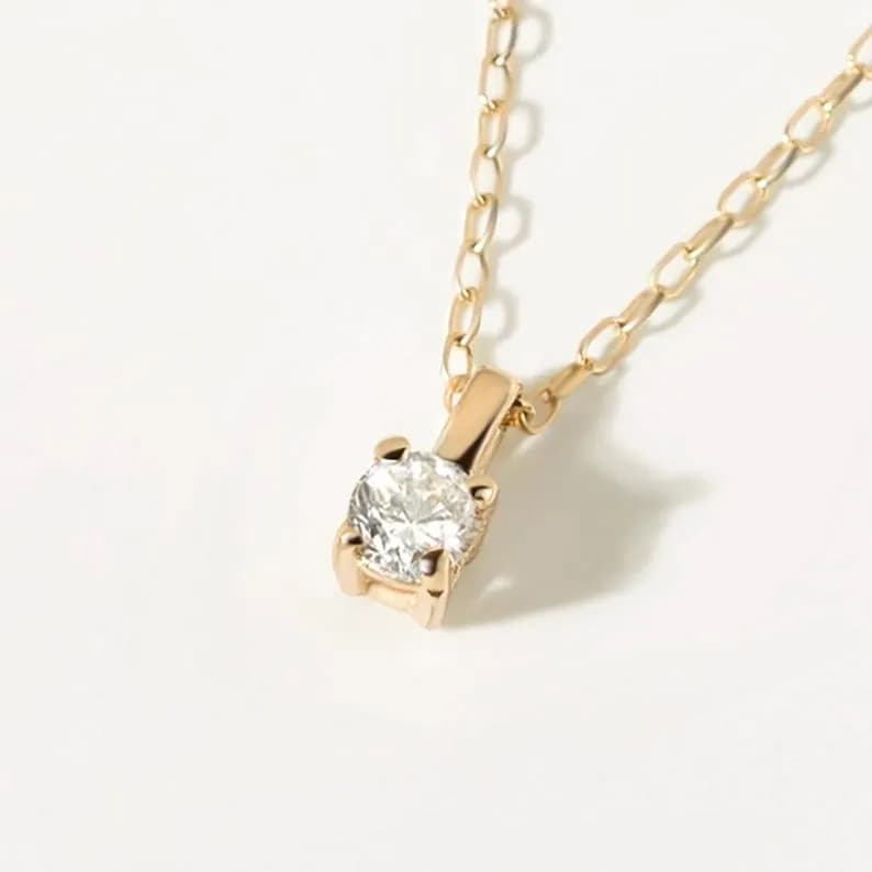 Gold diamond solitaire necklace with a round gemstone pendant, delicate chain design.