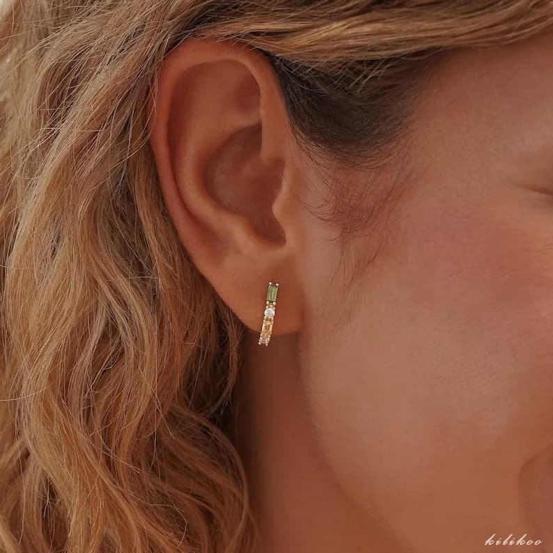 Gold-toned earring with colorful gemstones, worn on a blonde-haired person's ear.
