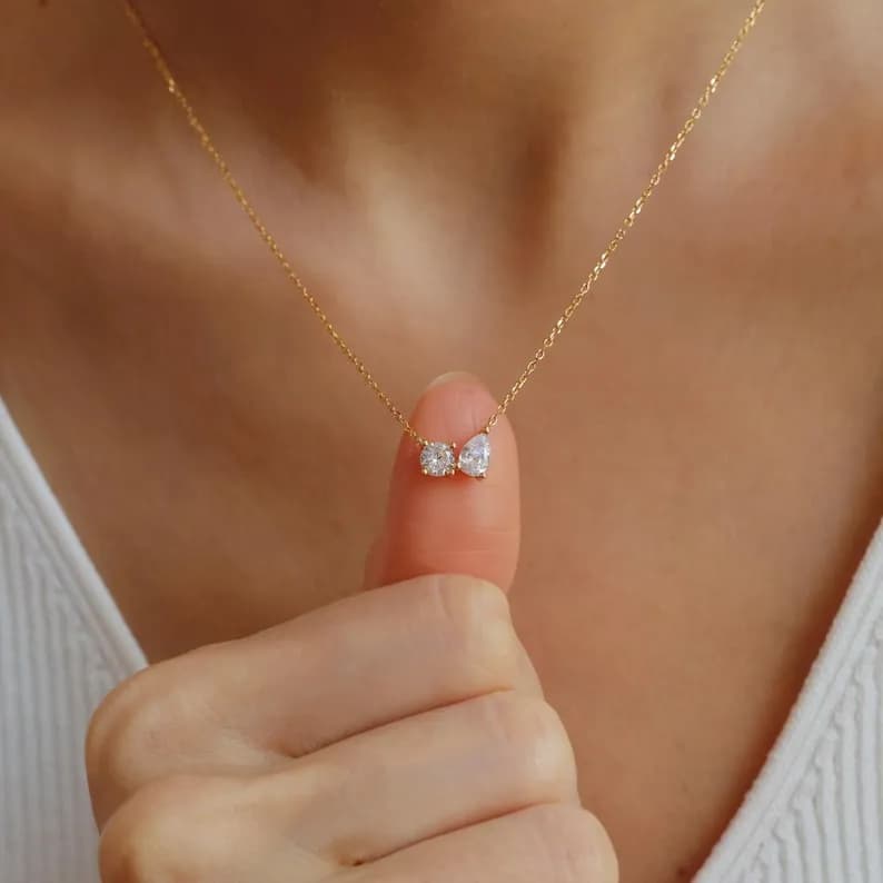 Delicate gold necklace featuring a small pendant with two clear, sparkling gemstones.