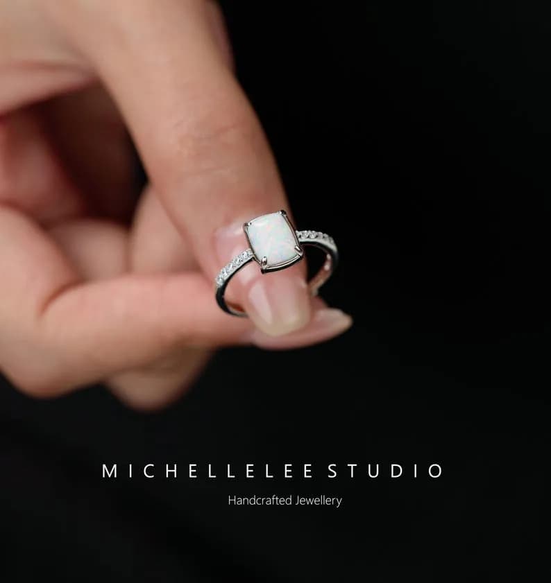 A silver ring with a rectangular, white opal gemstone, adorned with small, clear gemstones.
