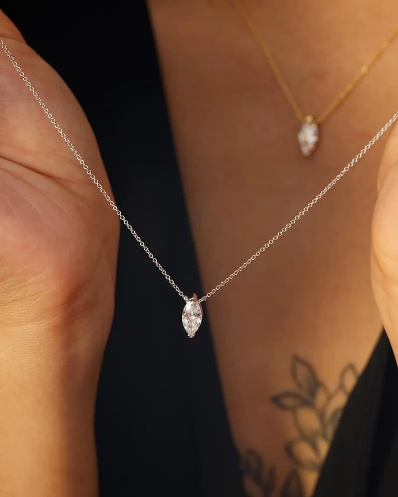 A silver necklace with a marquise-cut diamond pendant, worn by a person against a dark background.