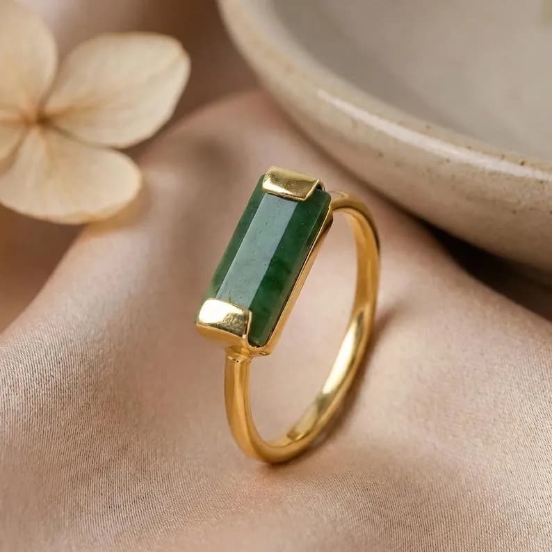 Gold ring with a rectangular, emerald-green jade stone, displayed elegantly.