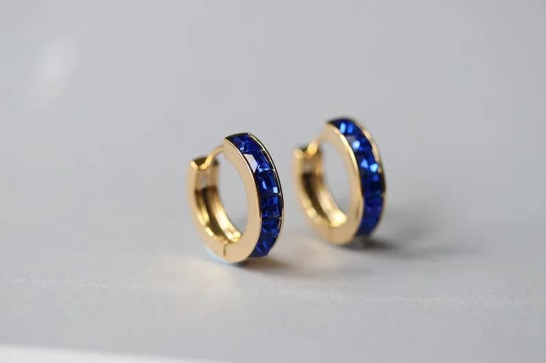 Gold hoop earrings with a row of blue gemstones around the hoop.